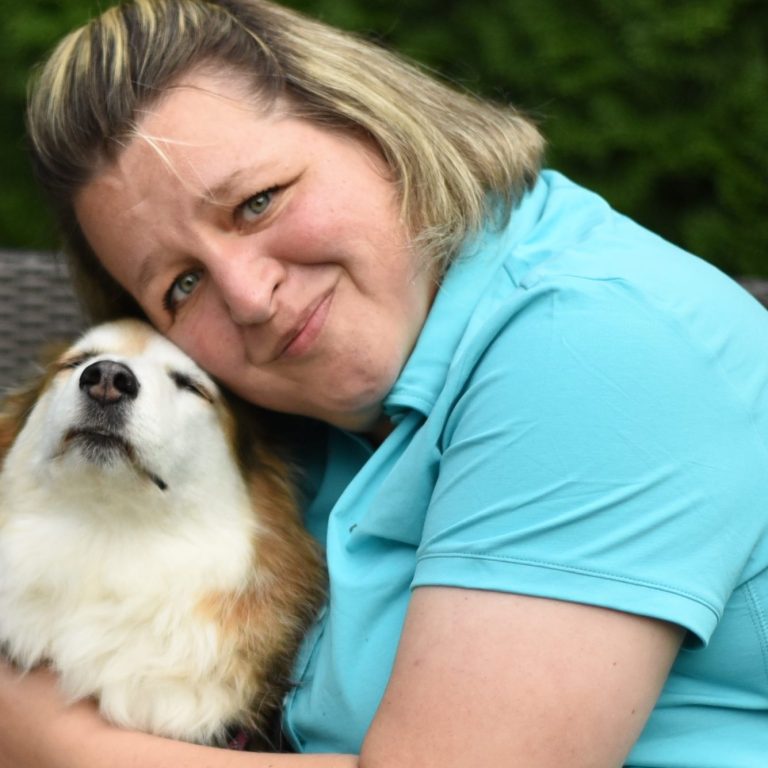 EineTierphysiotherapeutin umarmt einen Hund, beide wirken entspannt und freundlich. 