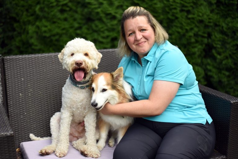 Protrait der Tierphysiotherapeutin mit Hunden Zertifizierte Tierphysiotherapeutin in professioneller Kleidung, freundlich lächelnd, vor einem neutralen Hintergrund.